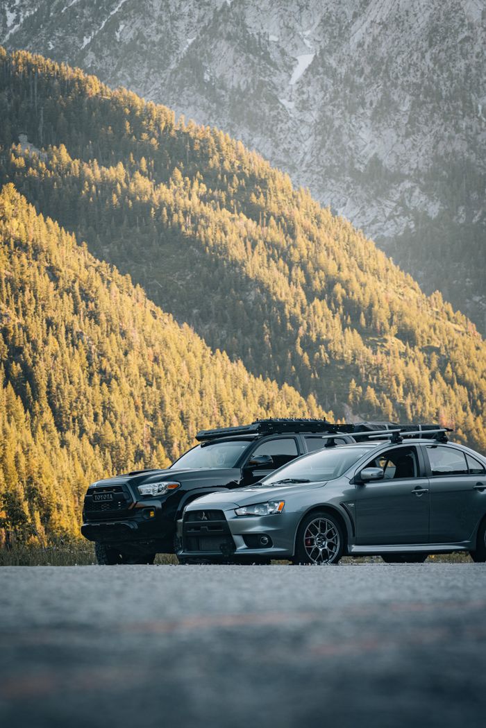 services-02 Two cars parked in a sunlit mountain setting, highlighting adventure and outdoor travel.