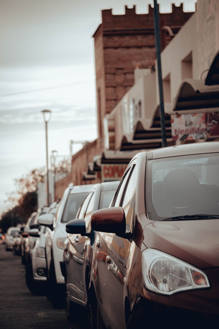 gallery-6 City street featuring parked cars with urban buildings in the background, showcasing traffic and city life.