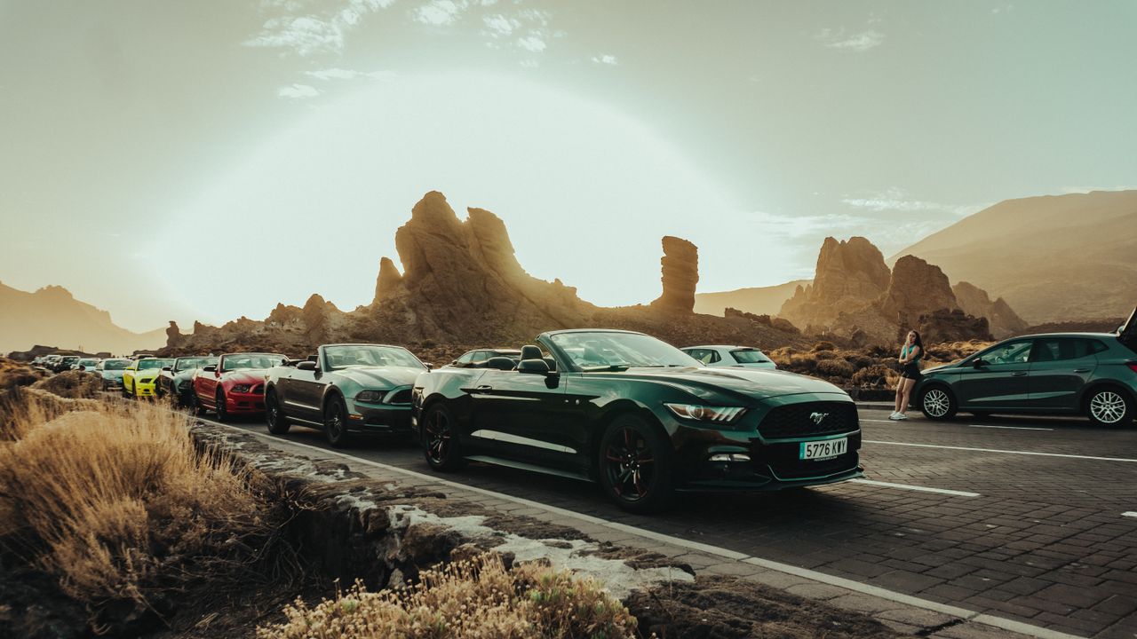 about-01 Cars lined up on a scenic road with striking rock formations during sunset.